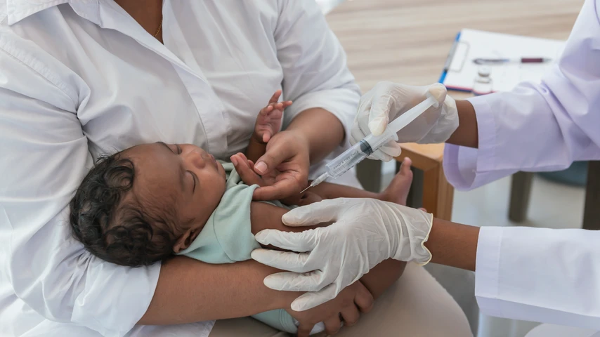 Baby lying in woman's arms, health professional administering a needle